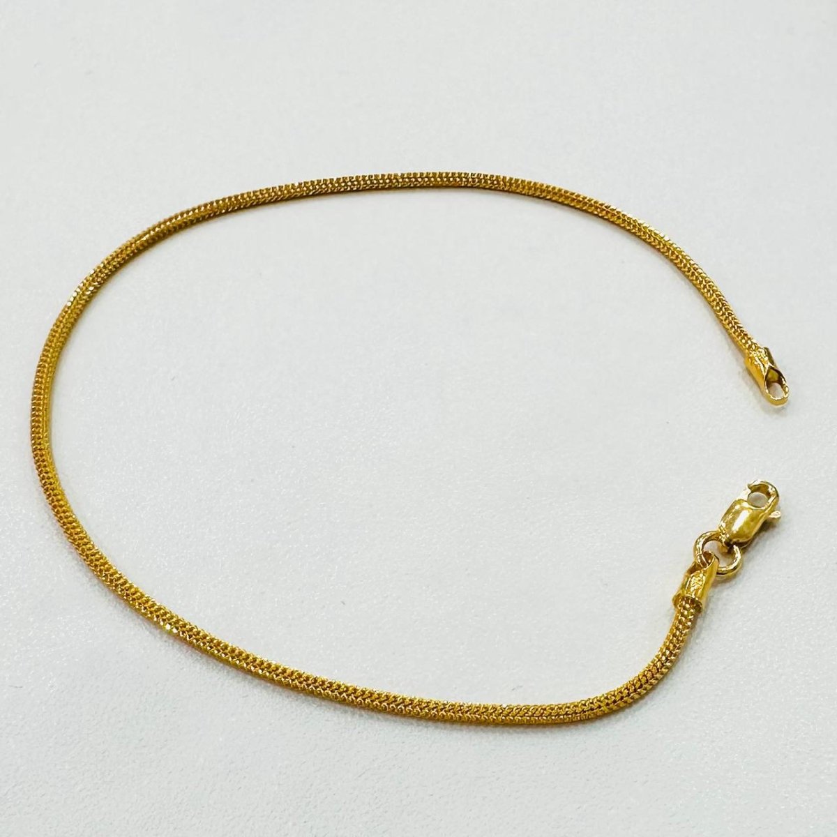 Full view of the 916 gold dragon-link chain bracelet arranged in an open oval on white fabric, with the lobster clasp at the lower right