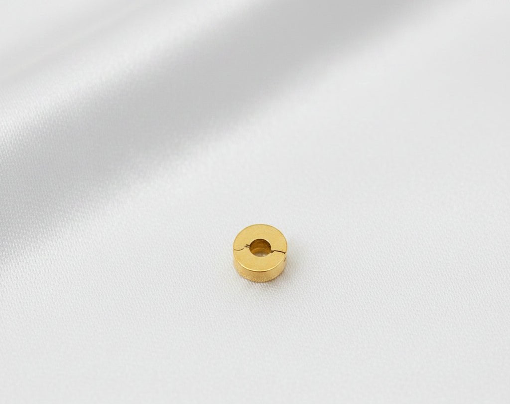 Top view of the round end of the 916 gold bracelet stopper charm, showing its central circular opening on white fabric