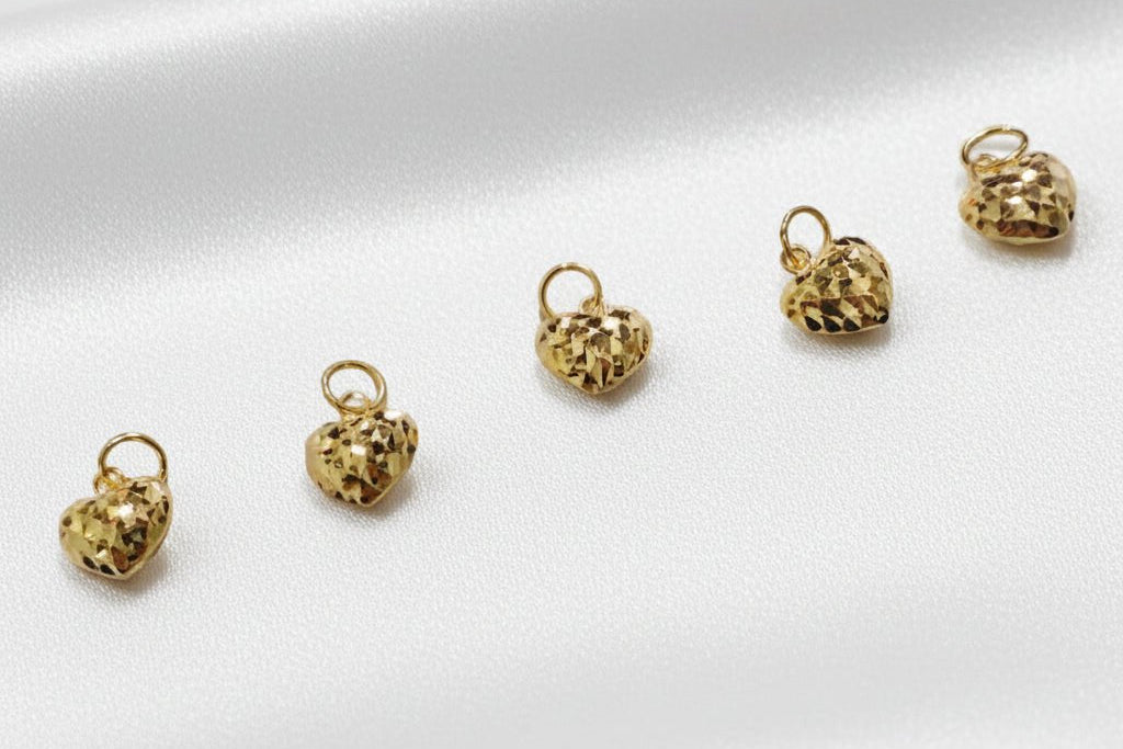 Five 916 gold diamond-cut heart charms arranged across white satin, with individual round attachment loops and faceted surfaces