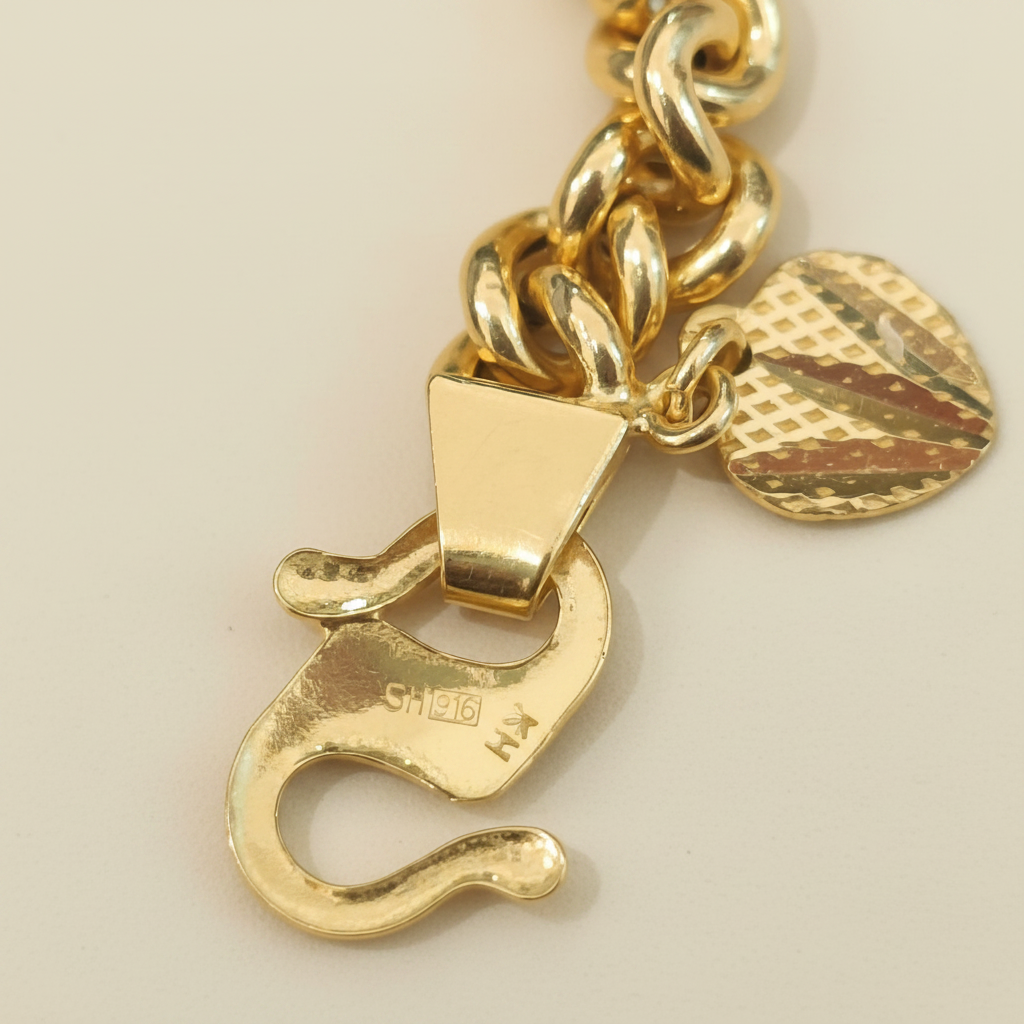 Close-up of the fishbone tube bracelet hook clasp with visible 916 stamp, curb-chain links and patterned heart-shaped tag