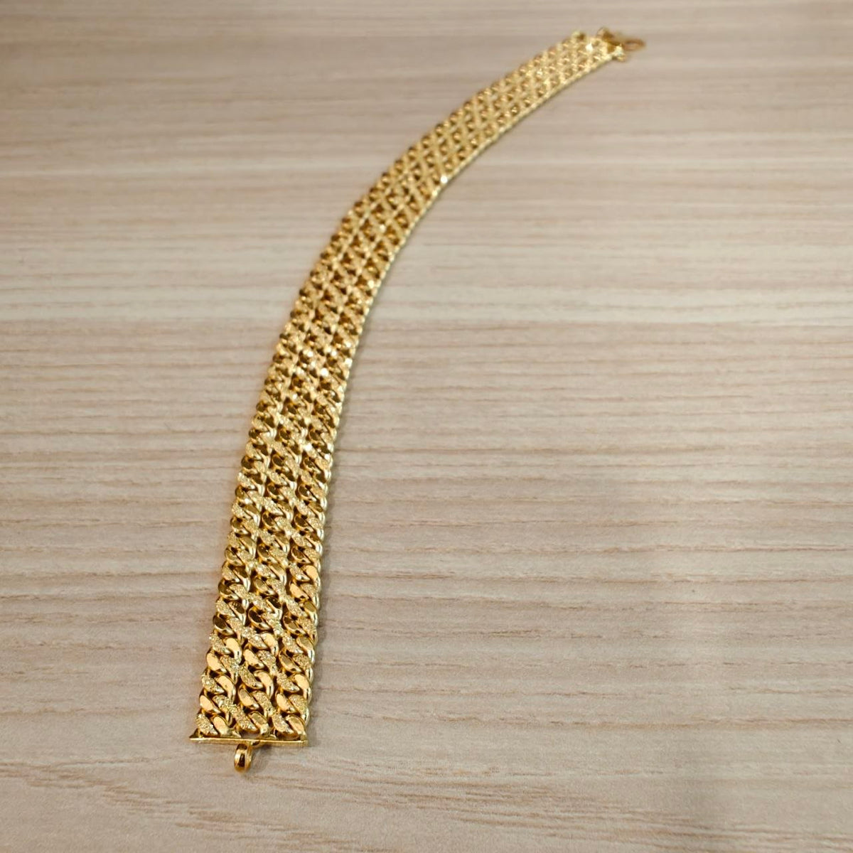 Full length of the 916 gold Triplet Cowboy bracelet laid in a gentle curve on wood, showing three rows of links and the end loop
