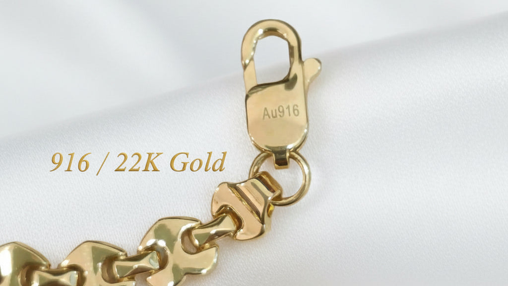 Close-up of the Metric Heart bracelet lobster clasp with visible Au916 stamp, connecting ring and polished gold links on white satin