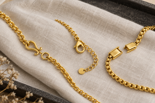 Three generic yellow-gold bracelet clasps arranged on ivory cloth: S-hook, lobster and box styles.