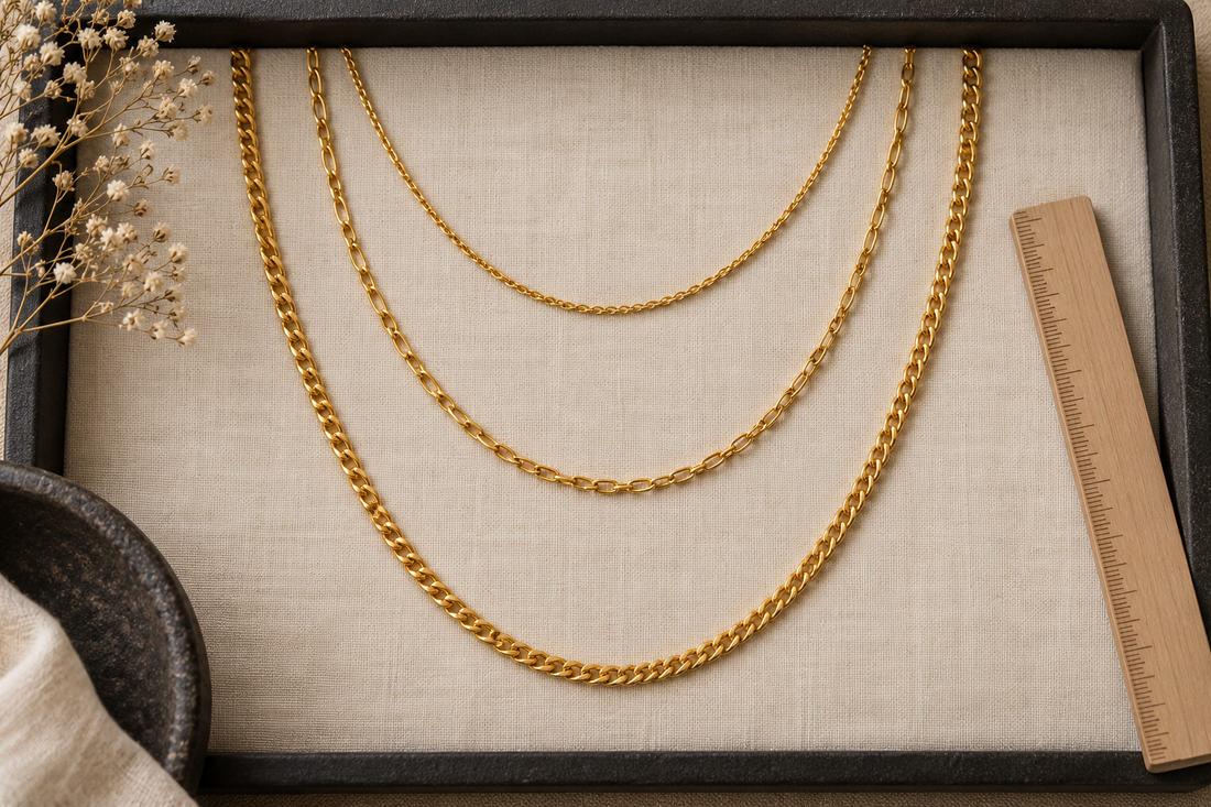Three generic yellow-gold necklace chains arranged in short, medium and long arcs beside a wooden ruler.