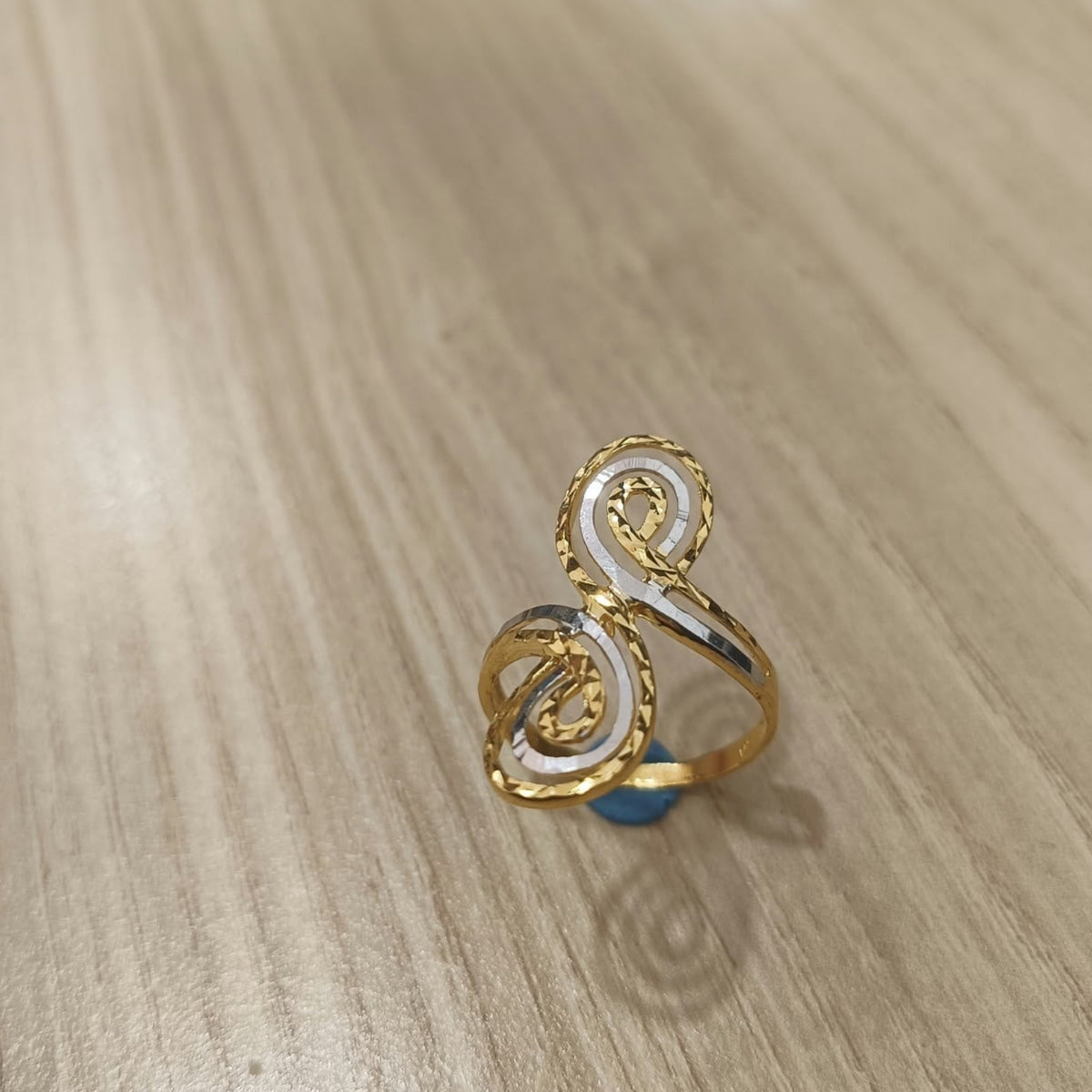 Angled view of a 916 gold two-tone swirl ring showing silver-coloured spiral accents and the gold band