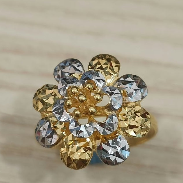 Front view of a 916 gold two-tone floral cluster ring with faceted petals on pale wood