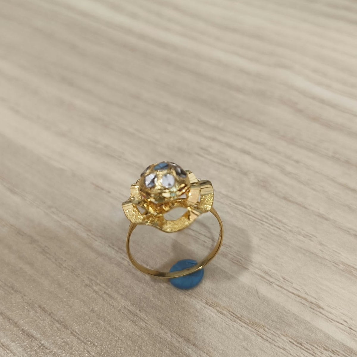 Angled view of a 916 gold two-tone lotus ring showing its layered flower design and gold band on pale wood
