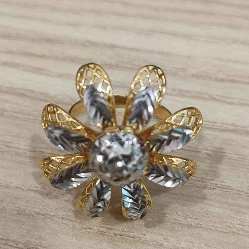 Front view of a 916 gold two-tone daisy ring showing its rounded centre and patterned flower petals on pale wood