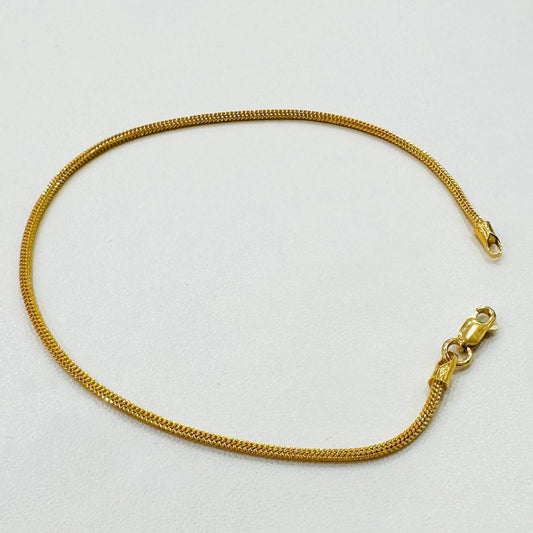 Full view of the 916 gold dragon-link chain bracelet arranged in an open oval on white fabric, with the lobster clasp at the lower right