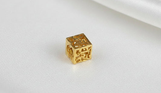 Full 916 gold cube stopper charm on white fabric, with patterned front and top faces and a circular side opening visible