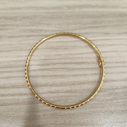 Detailed view of geometric diamond-cut facets on the gold bangle