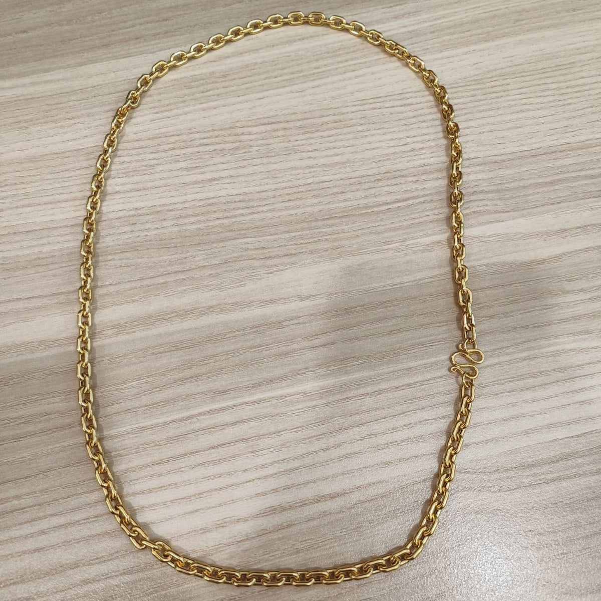Full oval view of the 916 gold hollow Wanzi chain on wood, showing the polished links and side-positioned S-hook clasp