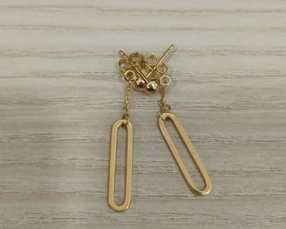 Pair of 916 gold paperclip dangle earrings with elongated open drops, short chains and round stud tops on a wood surface