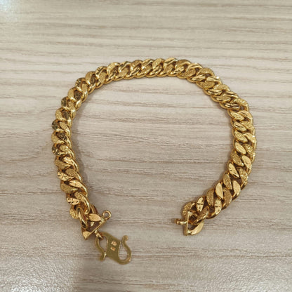 Cowboy-link gold bracelet arranged with open ends on a wood-grain surface