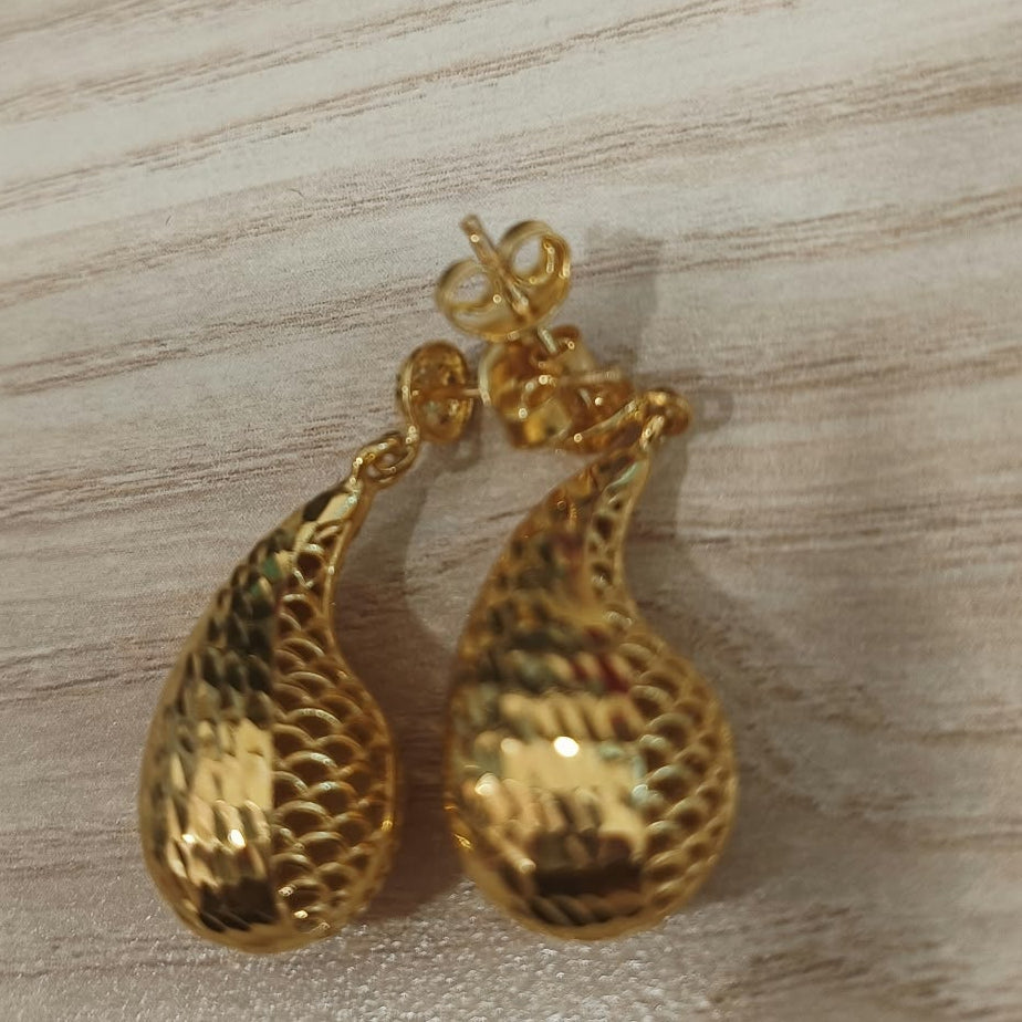 Front view of 916 gold teardrop earrings with faceted surfaces and openwork details on pale wood