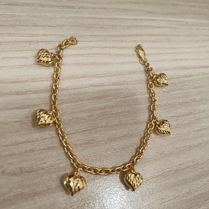 916 gold Wanzi six-heart bracelet laid in a U shape showing its chain, charms and clasp on pale wood