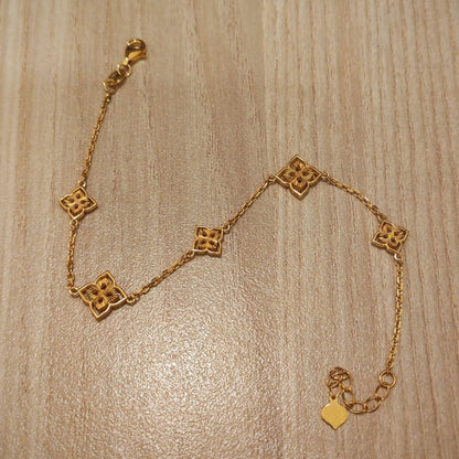 A delicate gold chain bracelet with five interlocking quatrefoil-shaped links, displayed on a light wood grain surface.