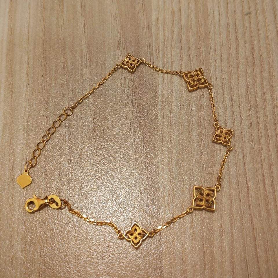 A delicate gold chain bracelet with five small interlocking quatrefoil-style links and a lobster clasp, displayed on a light wood grain surface.