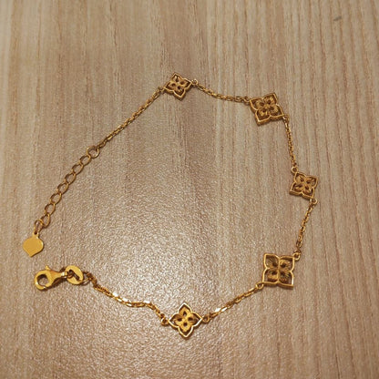 A delicate gold chain bracelet with five small interlocking quatrefoil-style links and a lobster clasp, displayed on a light wood grain surface.