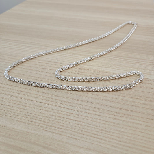 Complete 990 silver Spike chain necklace arranged in long curves on a light wood surface, showing the full chain and clasp